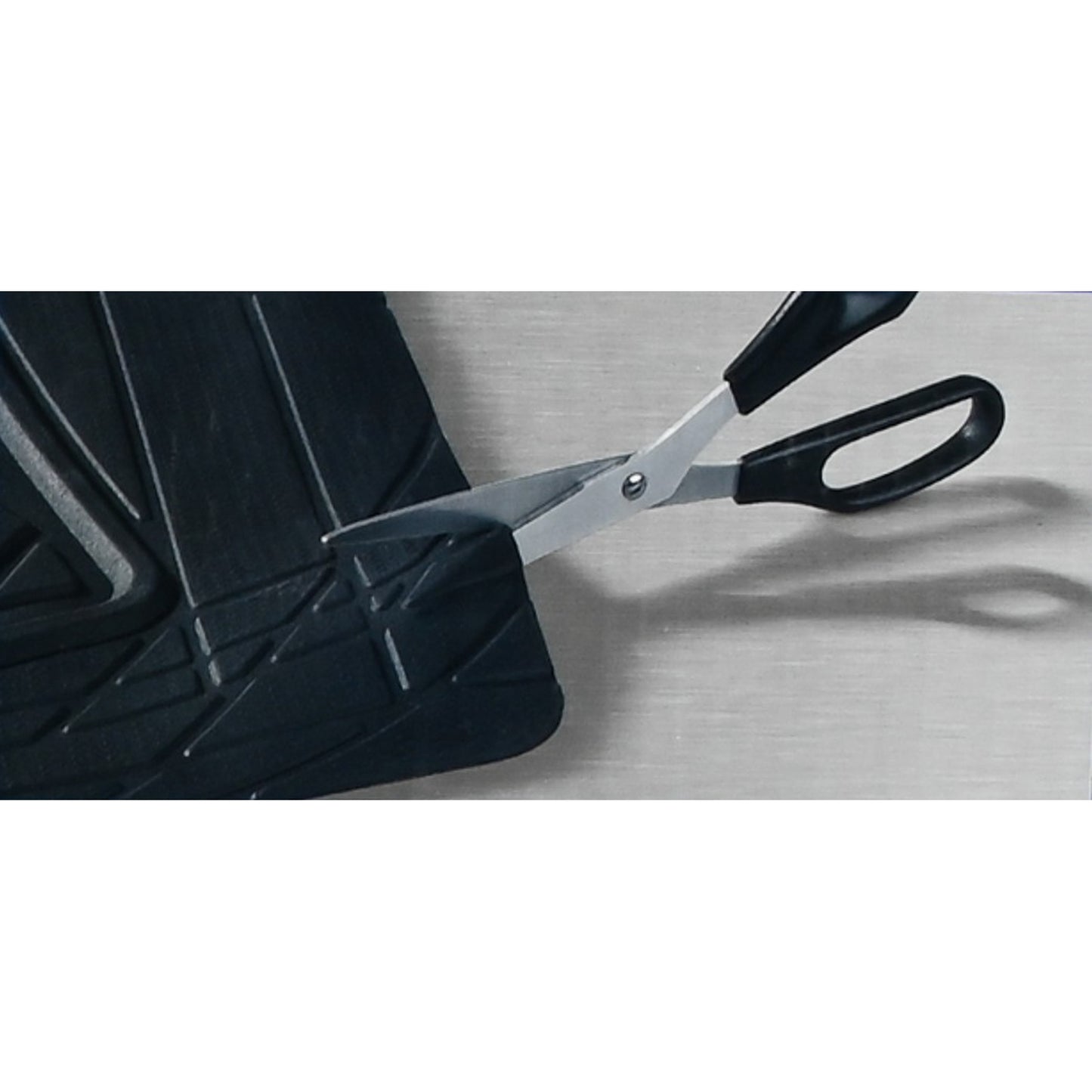 Teilansicht einer schwarzen Kofferraummatte, die mit einer Schere an der Kante zugeschnitten wird, auf grauer Oberfläche.