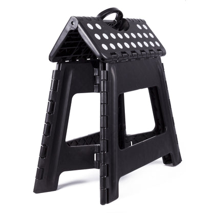 Zusammengeklappter schwarzer Klapphocker mit weißen Punkten auf der Sitzfläche und integriertem Tragegriff, stehend auf weißem Hintergrund.