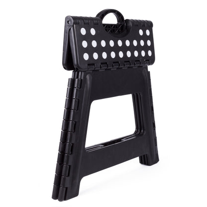 Zusammengeklappter schwarzer Klapphocker aus Kunststoff mit weißen Punkten auf der Sitzfläche und Tragegriff oben, seitlich stehend auf weißem Hintergrund.