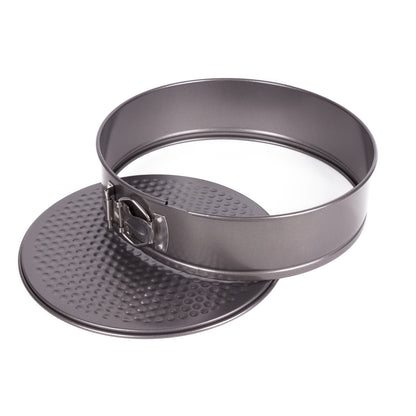Geöffnete runde Springform aus grauem Metall mit separat liegendem, strukturiertem Boden und gelöstem Spannring mit seitlicher Metallklammer, freigestellt vor weißem Hintergrund.