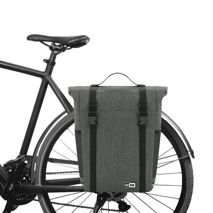 Graue Fahrradtasche mit Tragegriff und zwei Verschlussriemen, seitlich am hinteren Gepäckträger eines schwarzen Fahrrads befestigt.