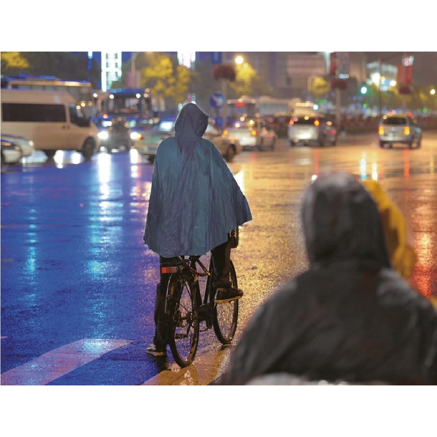 Person mit hellblauem Regenponcho fährt bei Regen auf einem Fahrrad durch eine nasse, beleuchtete Stadtstraße in der Nacht.
