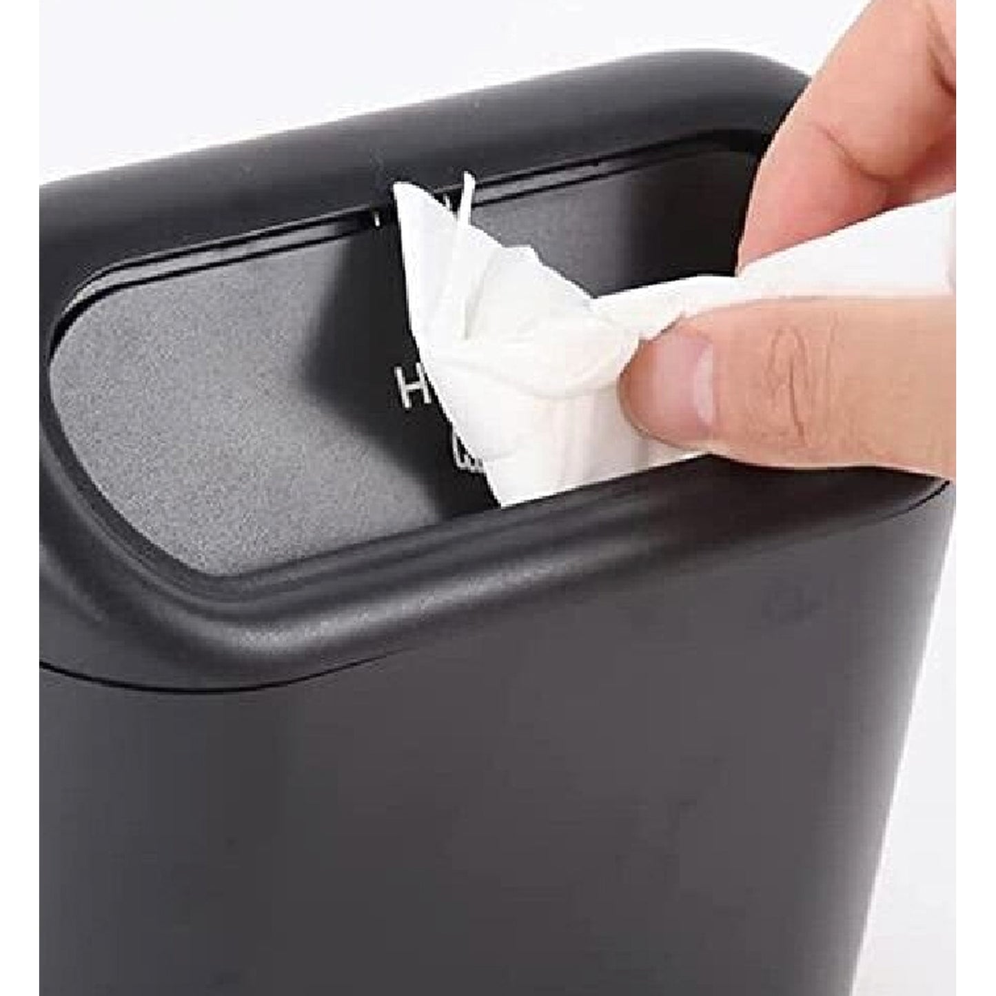Nahaufnahme eines schwarzen Auto-Mülleimers, eine Hand wirft ein zusammengeknülltes Papiertuch durch den Druckdeckel ein.