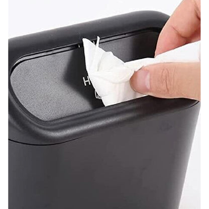 Nahaufnahme eines schwarzen Auto-Mülleimers, eine Hand wirft ein zusammengeknülltes Papiertuch durch den Druckdeckel ein.