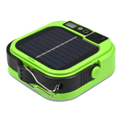 Grünes, kompaktes Solargerät in schräger Ansicht mit sichtbarer Solarzelle, Bedientasten, schwarzem Gehäuserand und eingehaktem Metallkarabiner, auf weißem Hintergrund.