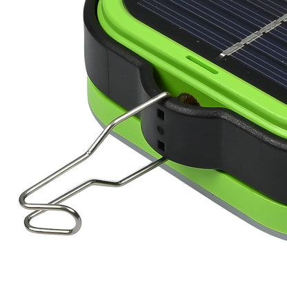 Detailansicht eines grünen Campinglichts mit schwarzem Gehäuserand, ausgeklapptem Metallhaken und sichtbarer Solarzelle, seitlich und nah aufgenommen vor weißem Hintergrund.
