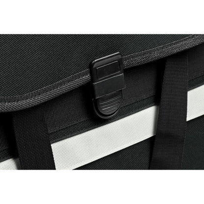 Detailaufnahme des schwarzen Steckverschlusses an der Vorderseite der Fahrradtasche mit grauem Reflektorstreifen darunter.
